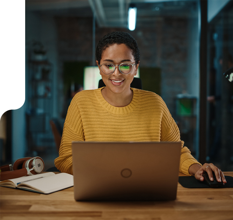 woman in a yellow sweater with glasses typing on laptop